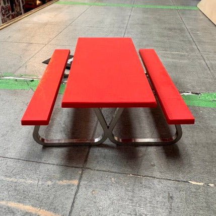 Red picnic table on a concrete floor with a skateboard ramp in the background